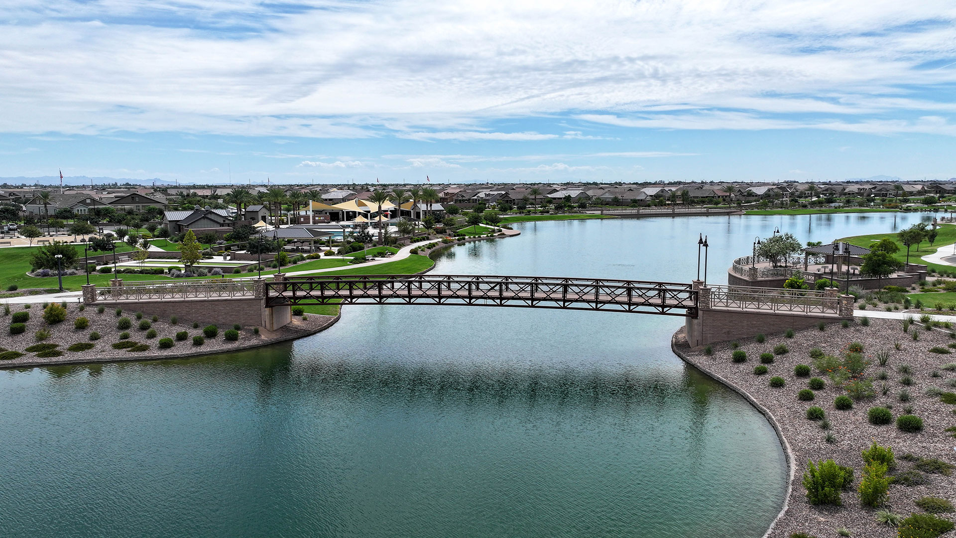 Aerial view of a Queen Creek master-planned community with a central lake and pedestrian bridge